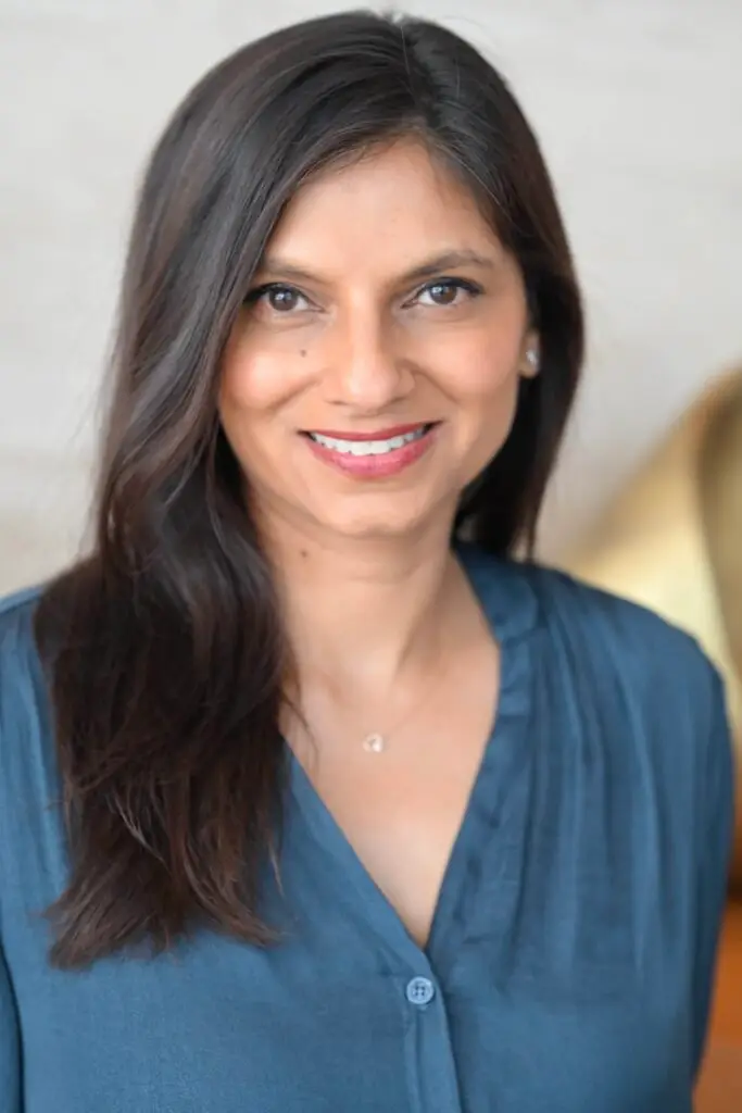 A smiling headshot of Dr. Monika Sharma wearing a blue shirt and looking at the camera. Dr. Sharma helps her clients overcome burnout and gain greater clarity, energy, and purpose.